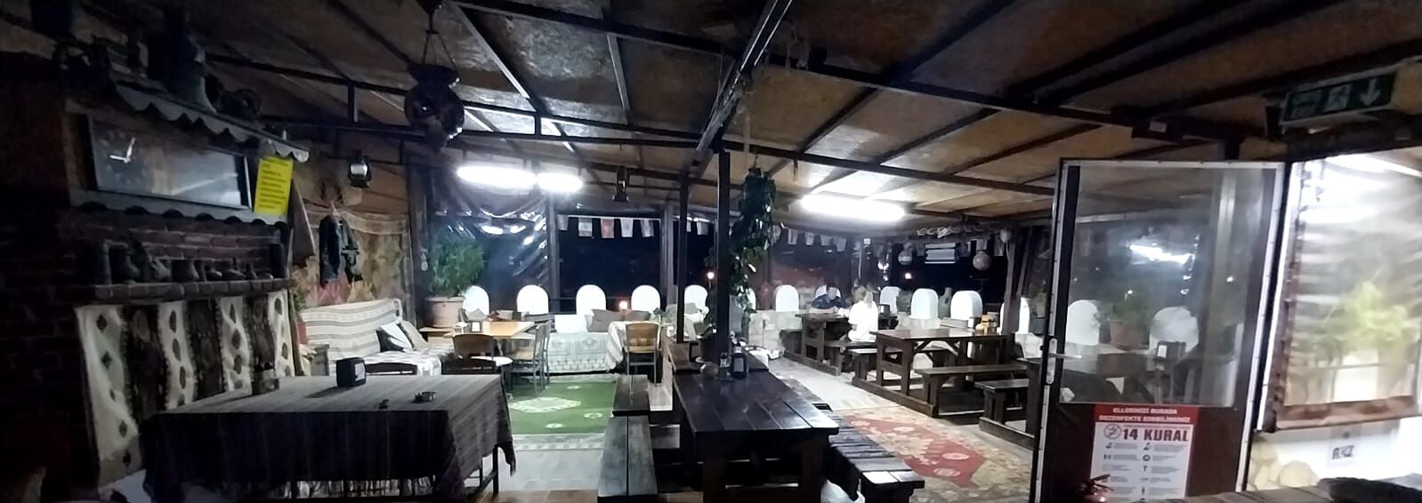 Un restaurante rústico con mesas y sillas de madera, una alfombra verde y un cartel que indica un precio de 14 KURA.