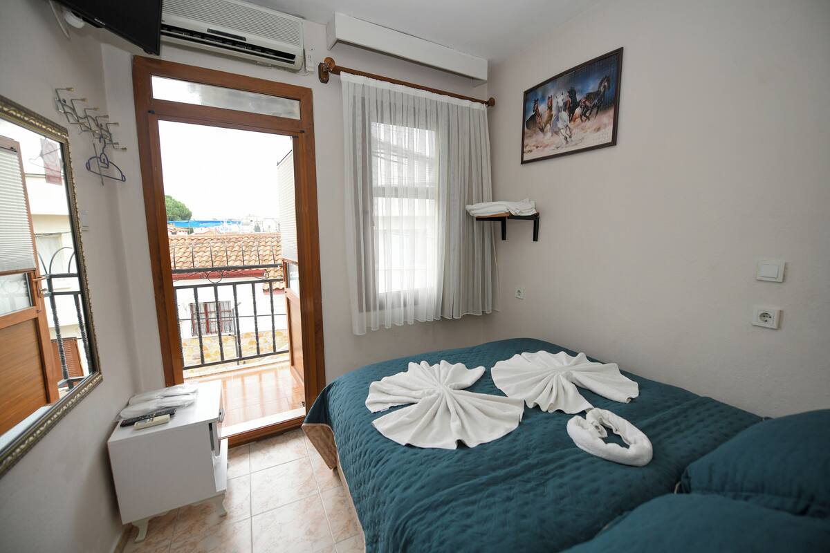 Ein Hotelzimmer mit Bett, Nachttisch, einem Fenster mit Vorhängen, einem Bild an der Wand und Blick auf den Balkon.
