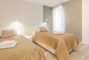 Ein Hotelzimmer mit zwei Betten, beigefarbener Bettwäsche, einem Nachttisch und einem Fenster mit Vorhängen.