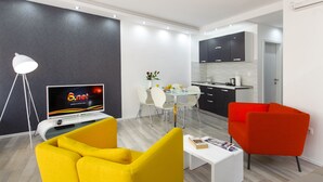 A modern living room with a TV, yellow and red chairs, a dining table with chairs, and a kitchen area. - Guest House Teatrin Split (Split)