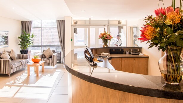 Un hall d'hôtel moderne avec un comptoir d'accueil incurvé, un coin salon avec des canapés à rayures, une plante en pot et un vase rempli de fleurs.