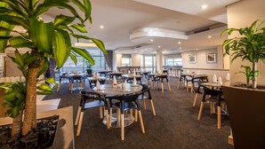 Un espace repas moderne avec des tables rondes, des chaises noires et des plantes en pot.