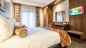 A hotel room with a large bed, a desk, a television, and a window with curtains.