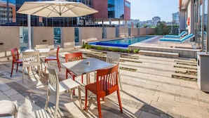 An outdoor patio with tables and chairs, a pool, and a view of the cityscape.