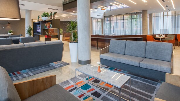 A modern lobby with seating areas, a reception desk, and large windows.