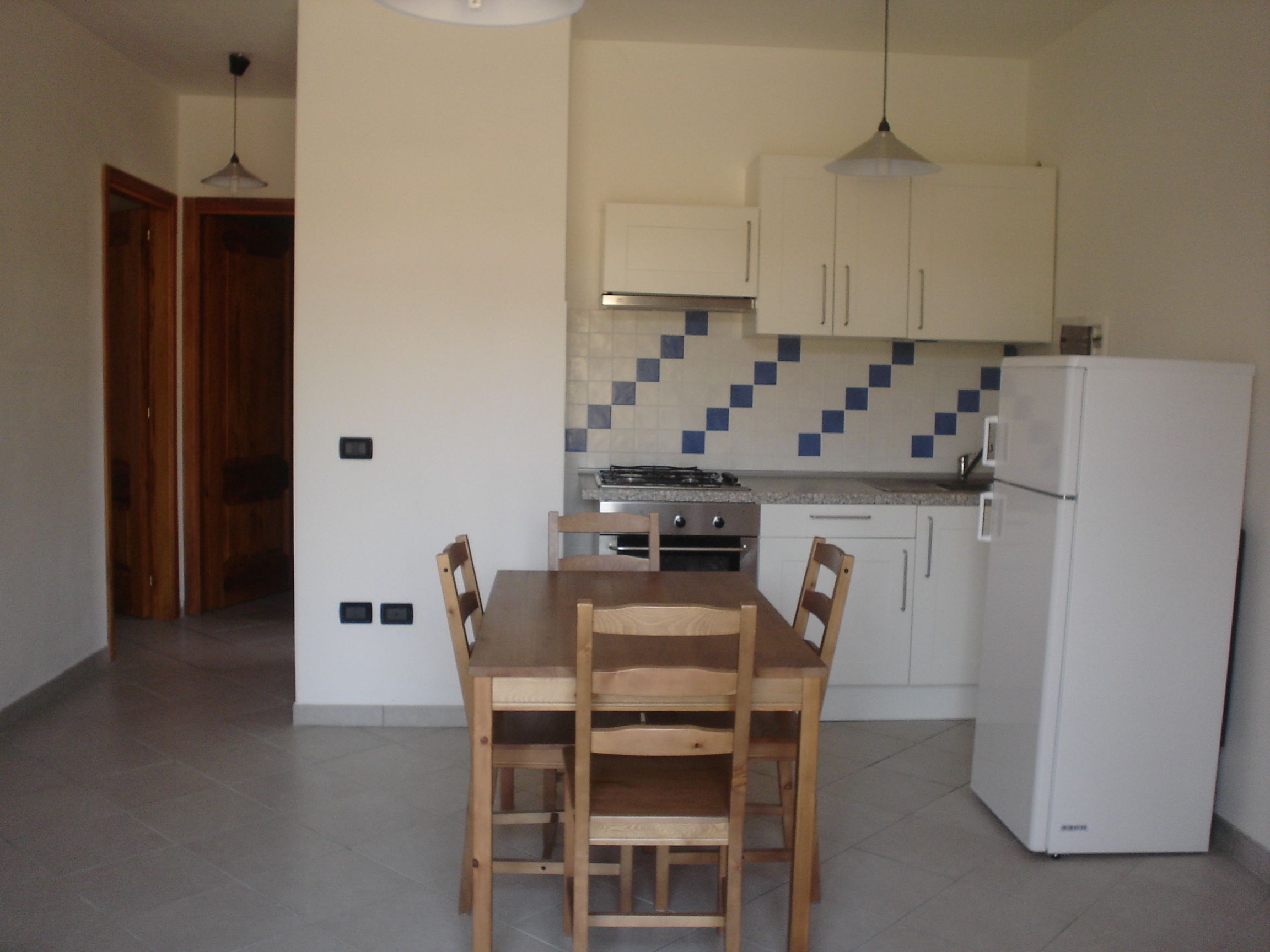 A compact kitchen with white cabinets, a tiled backsplash, a stove, and a refrigerator.
