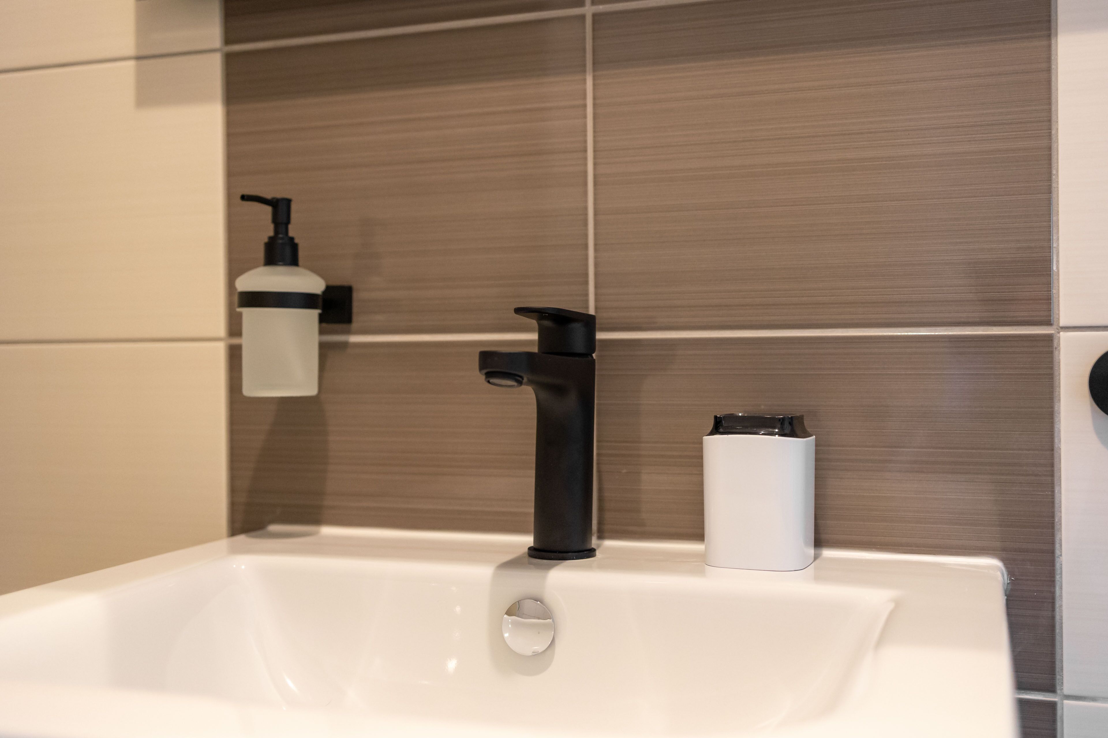 A bathroom sink with a black faucet, a soap dispenser, and a soap holder.