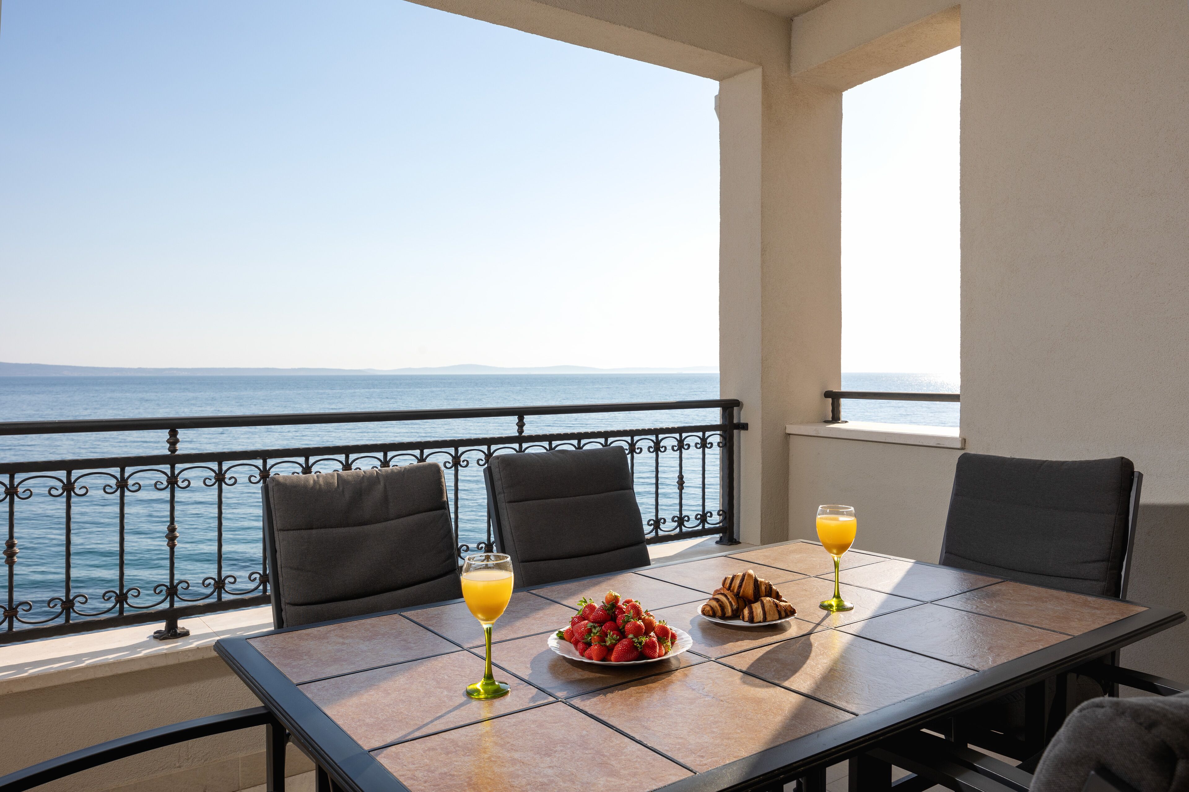 A balcony with a table set for breakfast, overlooking the sea.