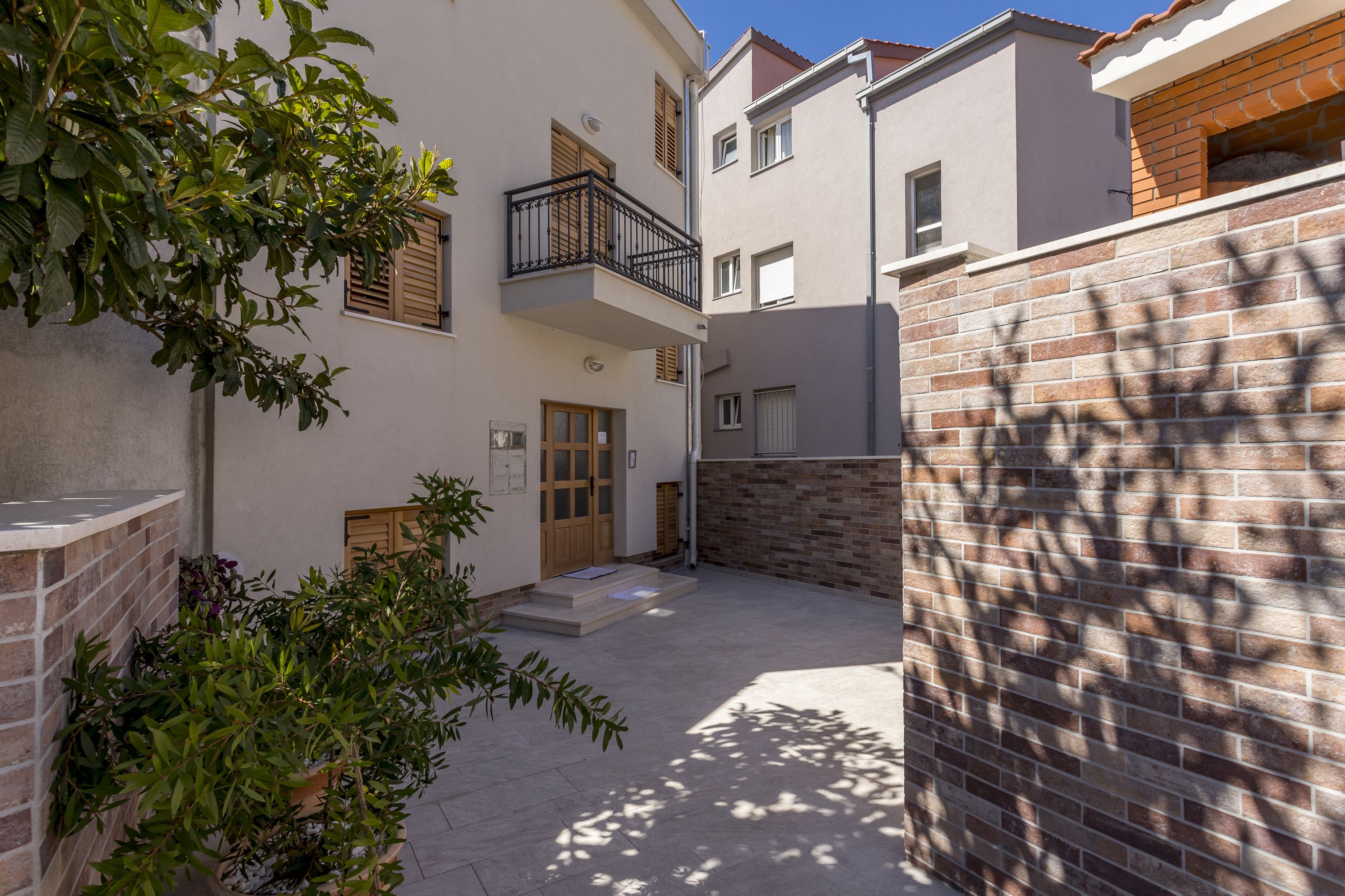 A courtyard with a brick wall, a wooden door, and a small balcony with a black railing.