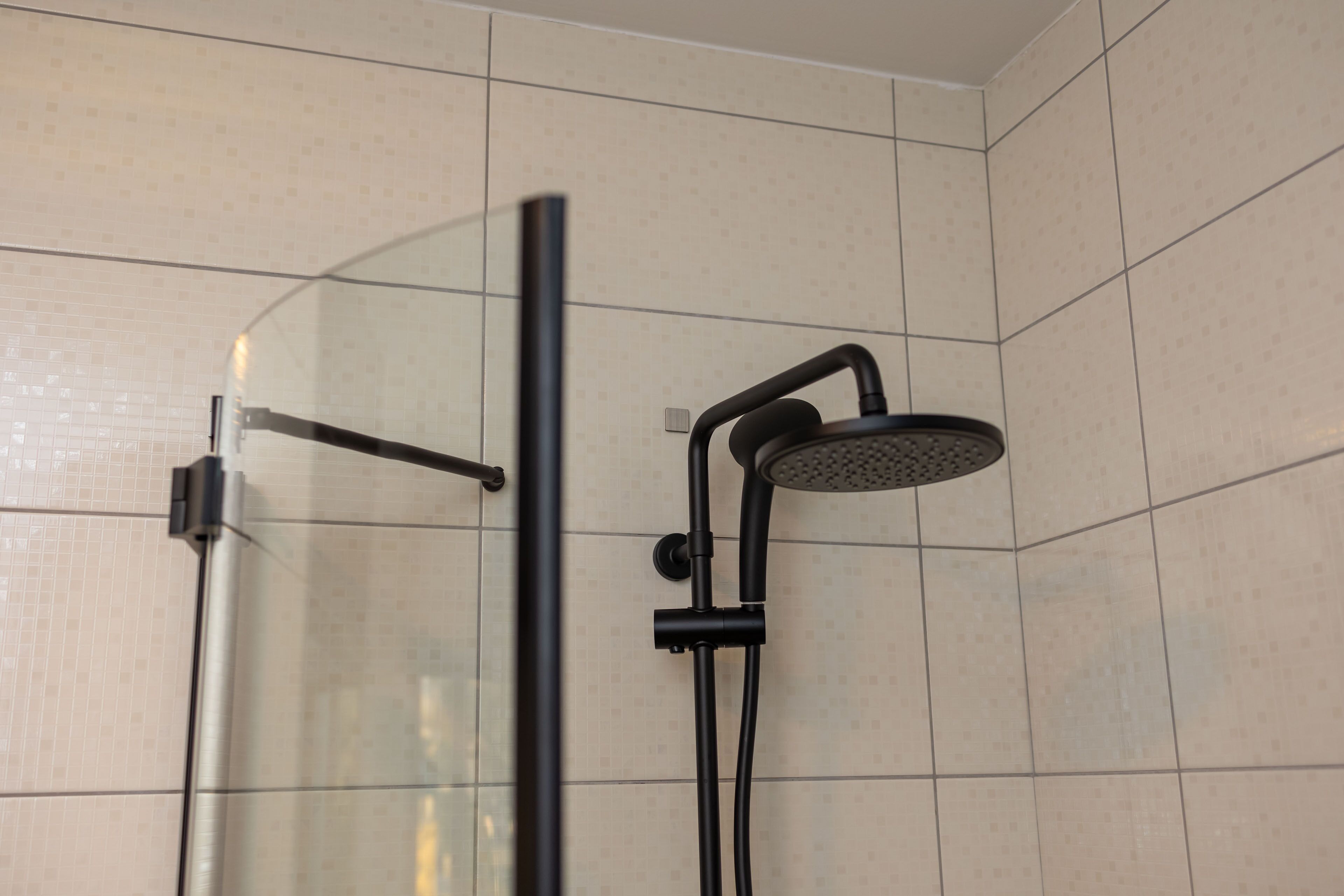 Een douchecel met glazen wanden, een handdouche en een bedieningspaneel aan de muur.