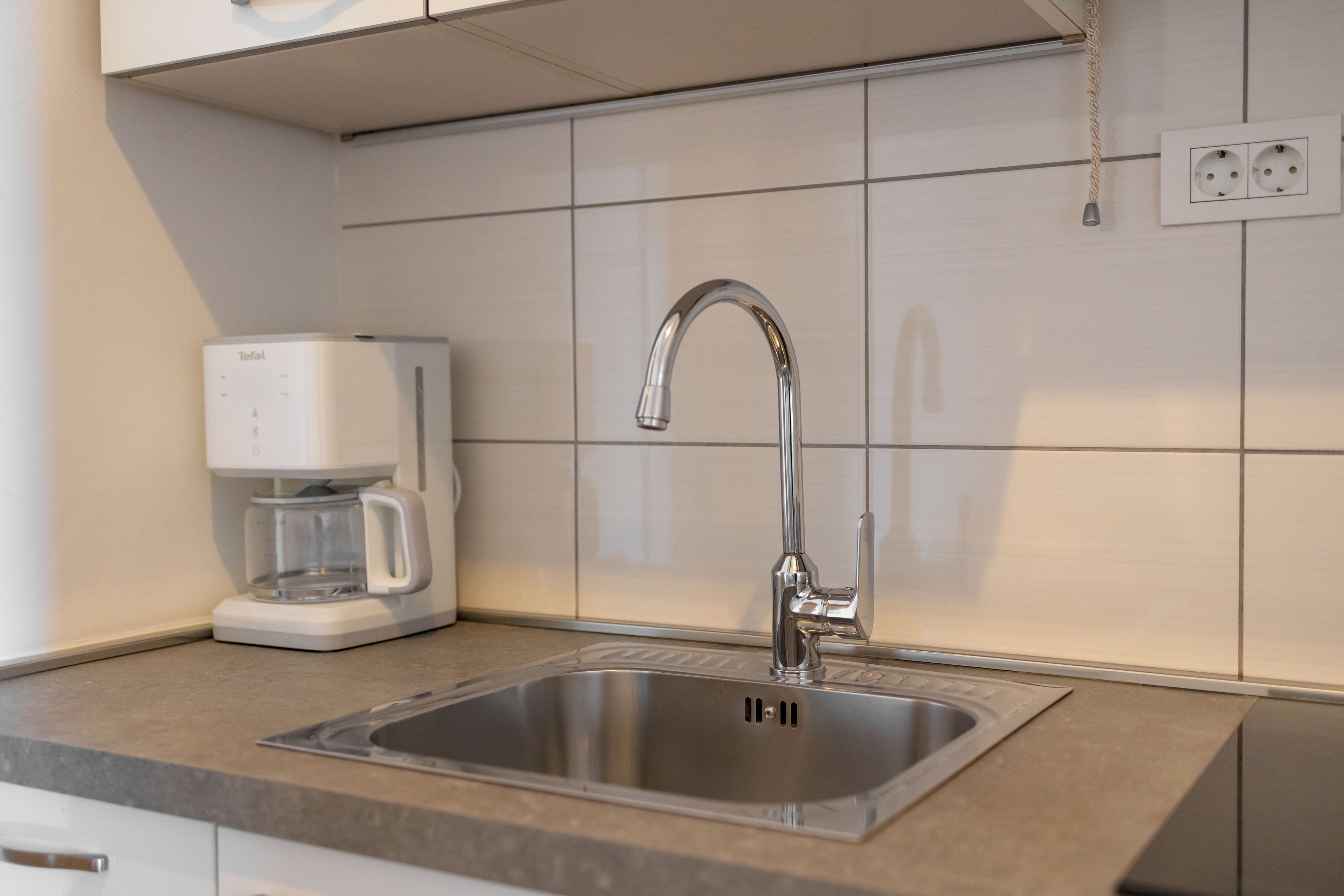 Eine Küche mit einem Edelstahlspülbecken, einer Kaffeemaschine und einer Wandsteckdose.