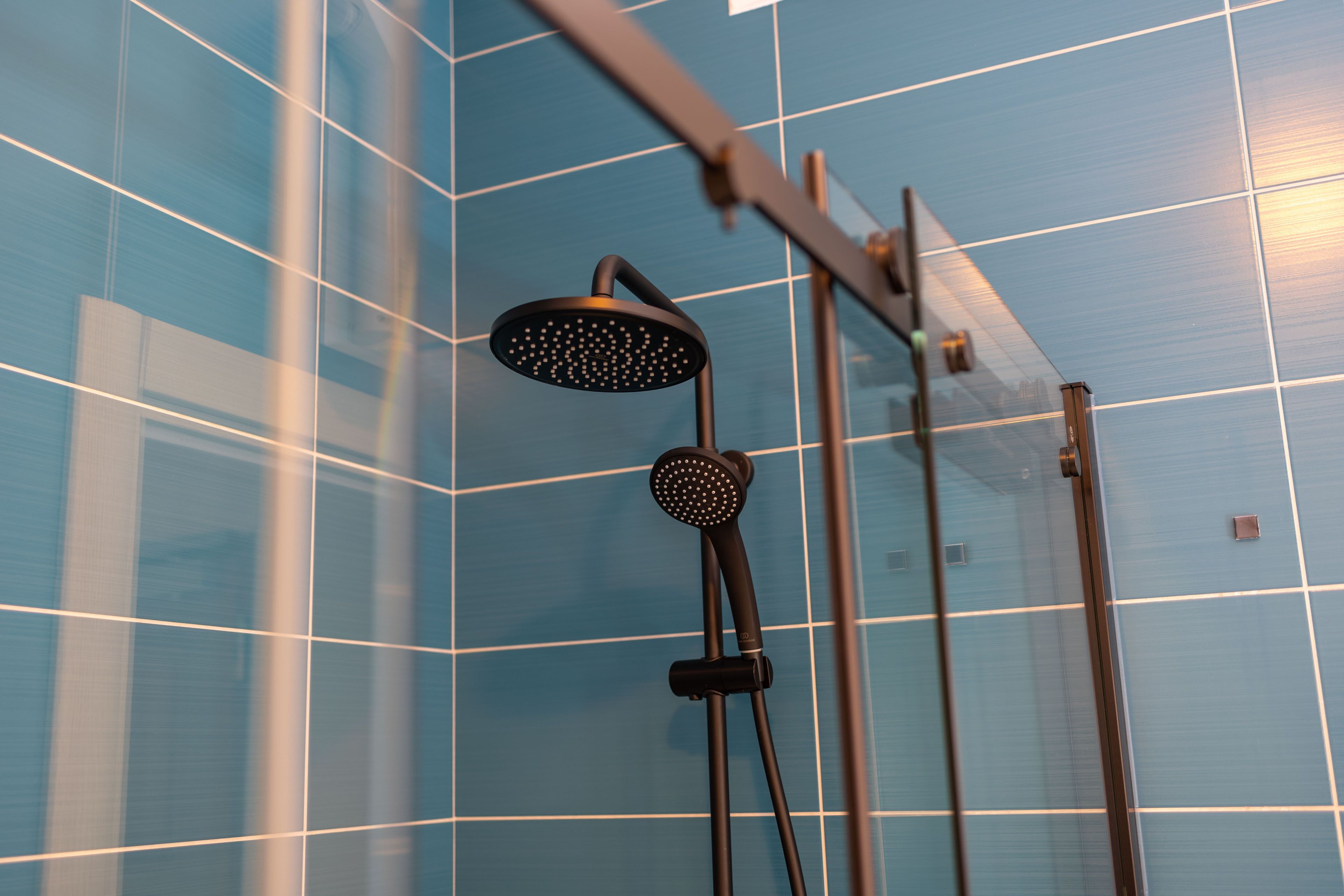 Een douche met een handdouche en een douchekoof, tegen een betegelde muur.