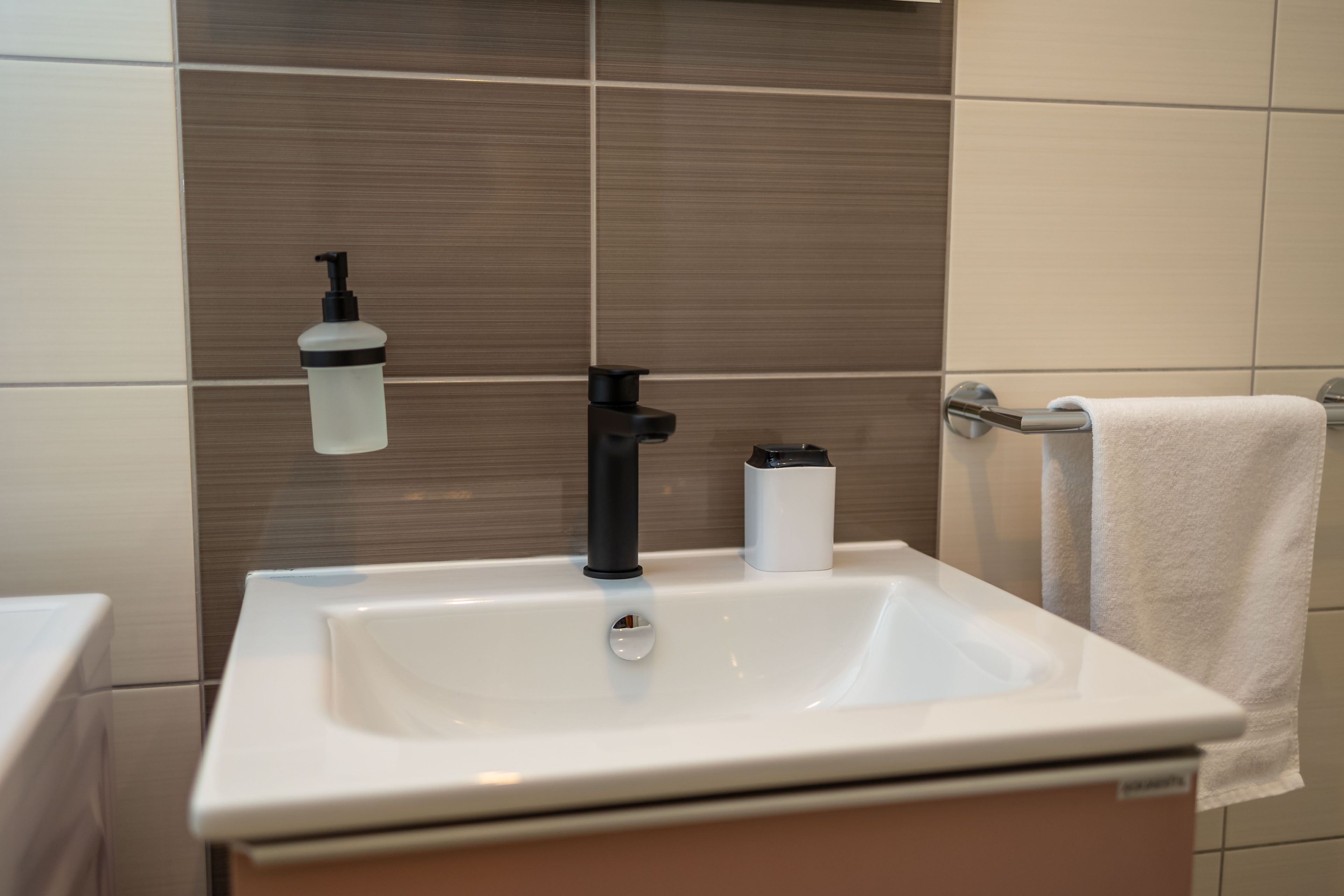 A bathroom with a white sink, black faucet, and a white towel hanging on a towel rack.