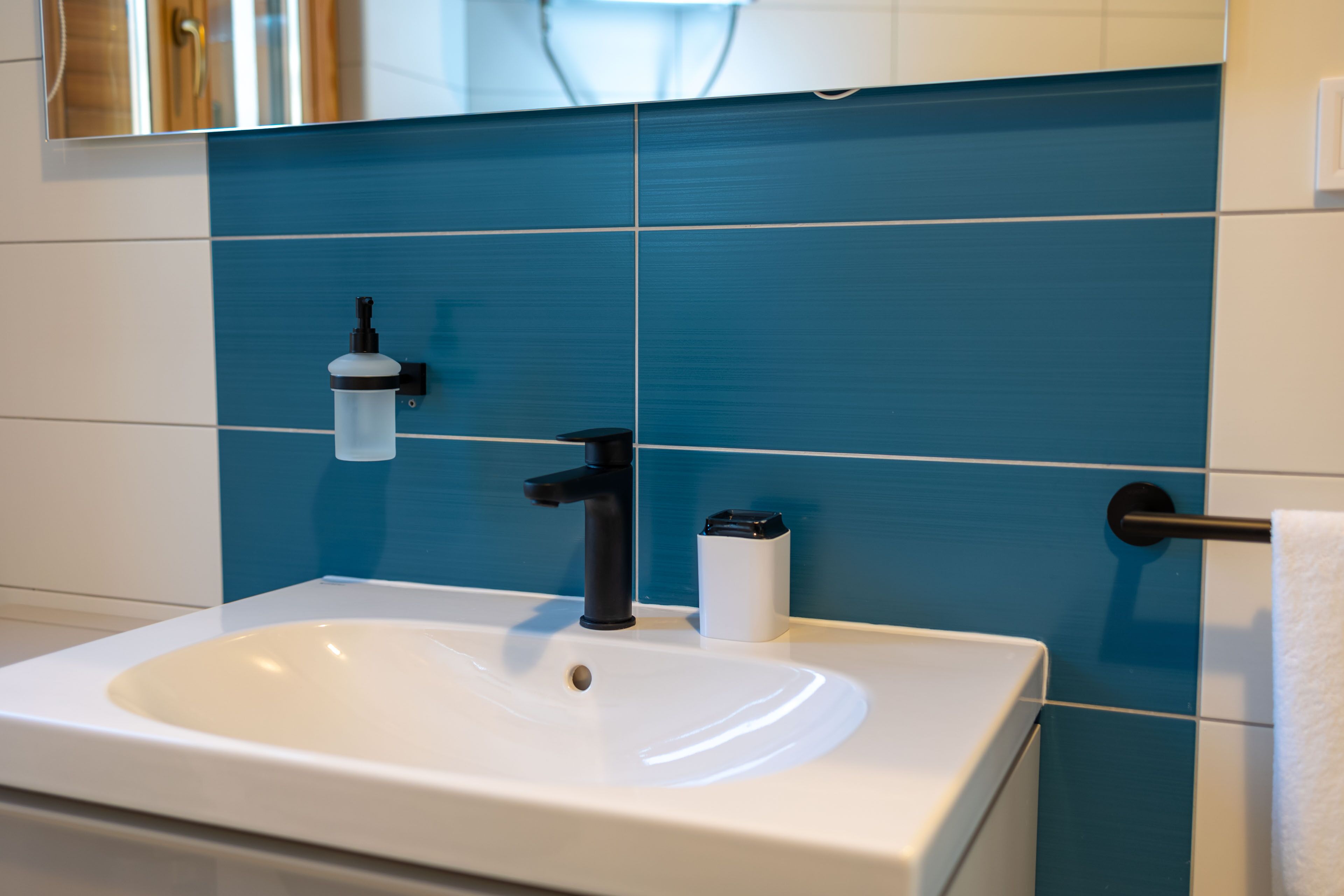 A bathroom with a white sink, a black faucet, and a blue tiled wall.