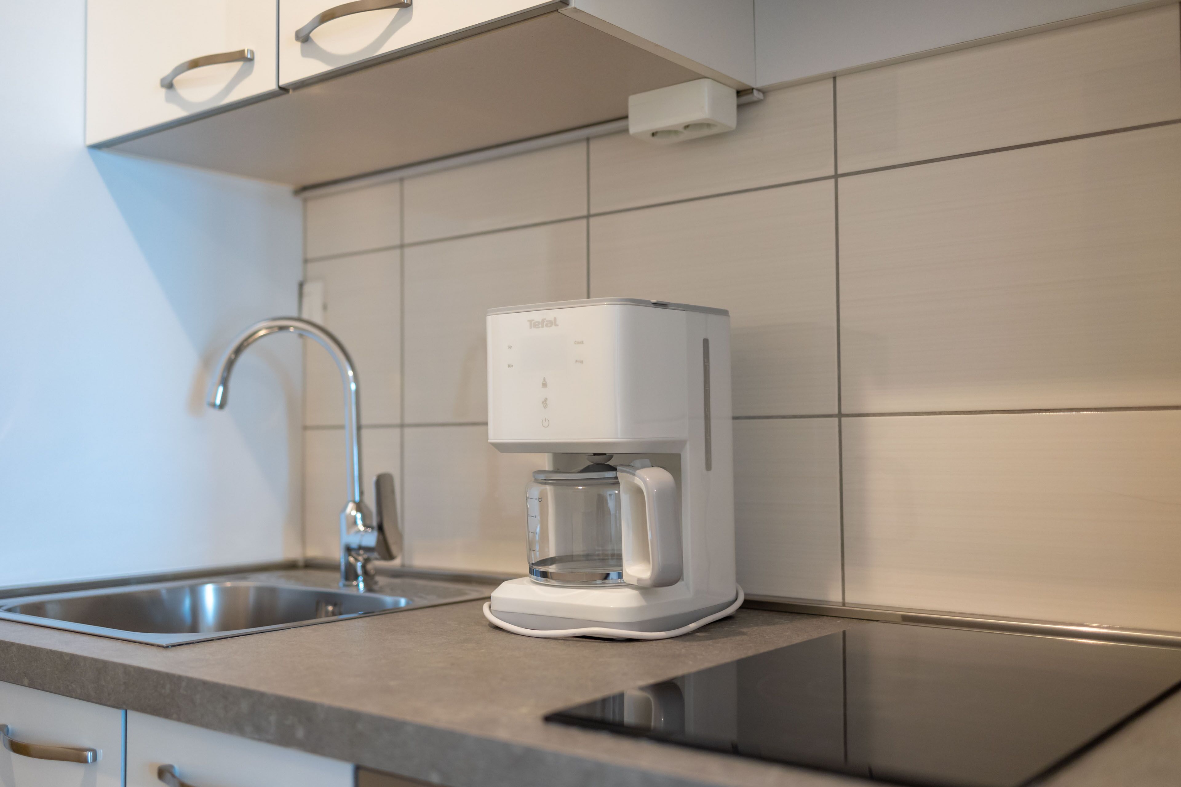 Una cocina moderna con cafetera integrada, pileta de acero inoxidable y alacenas blancas.
