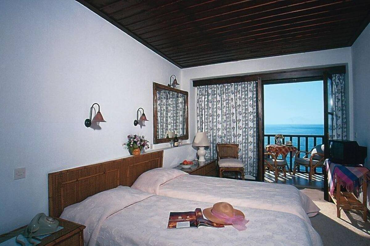 Ein Hotelzimmer mit Bett, Sessel, Tisch, Fernseher und einem Balkon mit Meerblick.