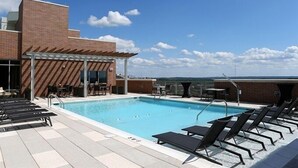 A rooftop pool with lounge chairs, a covered seating area, and a clear view of the city skyline. - Weichert Suites at Gallery Bethesda (Bethesda)