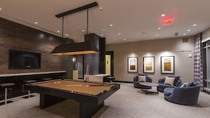 A pool table in a modern lounge area with a flat-screen TV, comfortable seating, and framed artwork on the walls. - Weichert Suites at Gallery Bethesda (Bethesda)