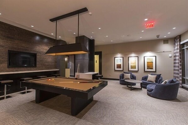 A pool table in a modern lounge area with a flat-screen TV, comfortable seating, and framed artwork on the walls.