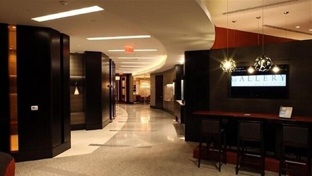 A hotel lobby with a reception desk, bar area, and a wall-mounted television displaying 'GALLERY'. - Weichert Suites at Gallery Bethesda (Bethesda)