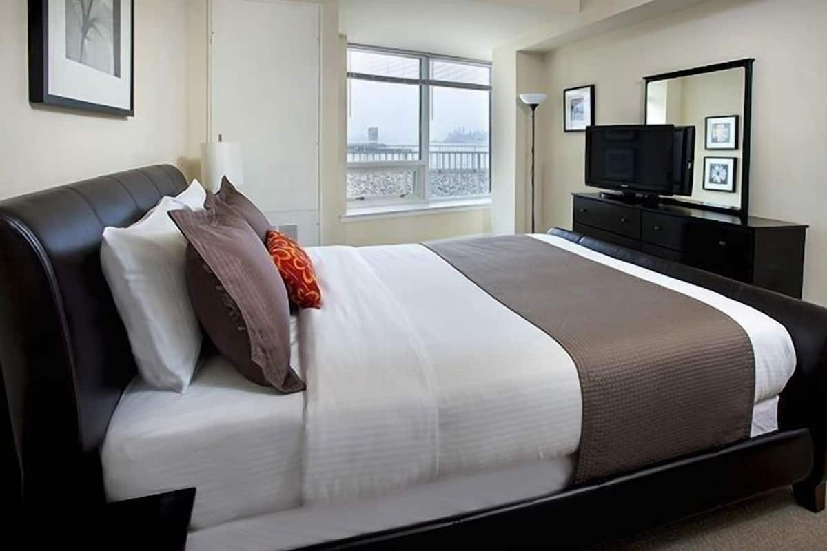 A hotel room with a large bed, a television, a dresser, and a window with a view.
