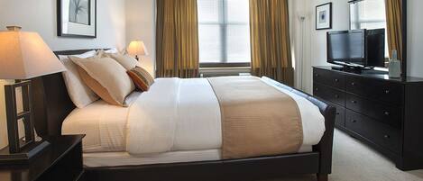 A neatly arranged hotel room with a large bed, bedside lamps, a flat-screen TV, a dresser, and a window with curtains.