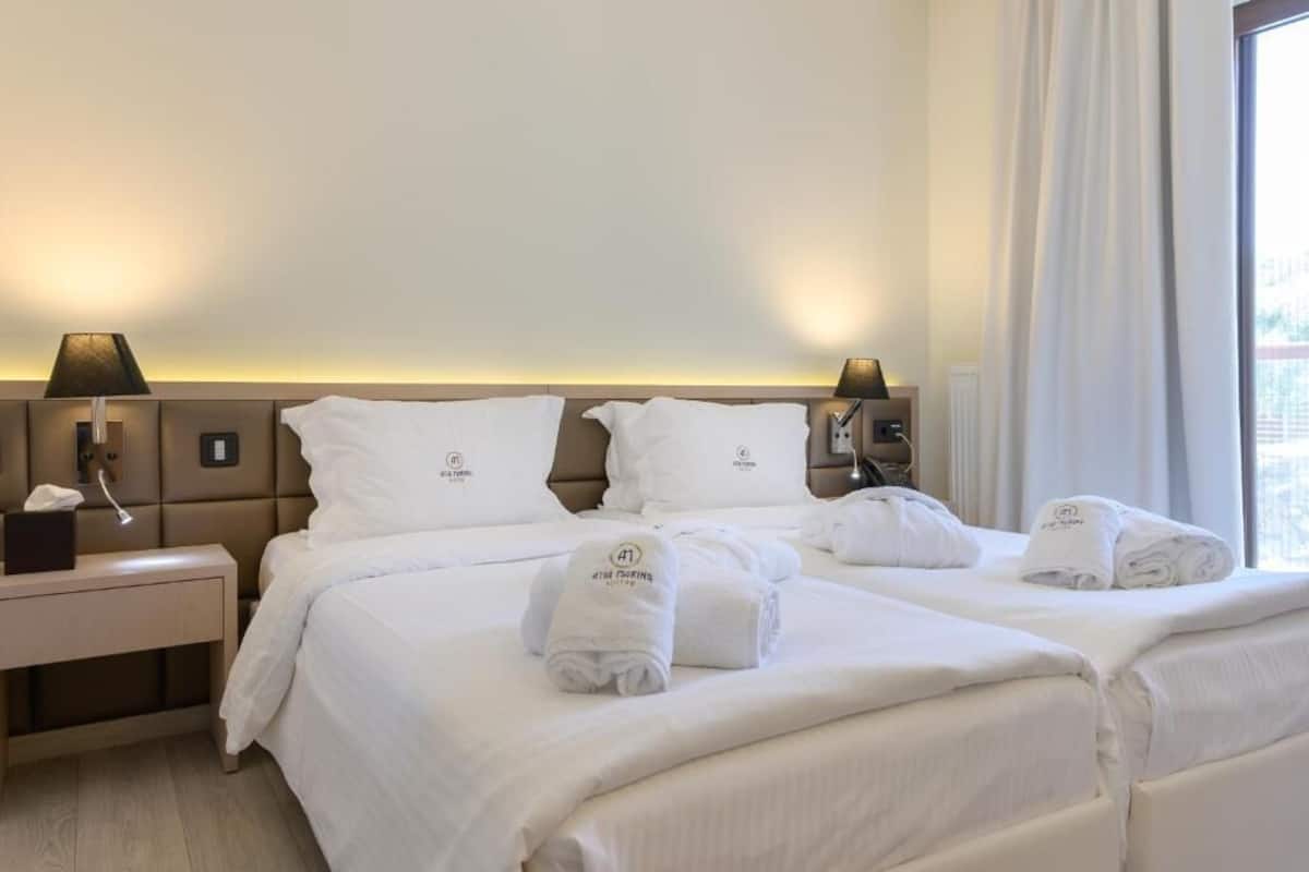 Ein Hotelzimmer mit einem großen Bett, zwei Nachttischen mit Lampen und einem fensterbelaubten Fenster.