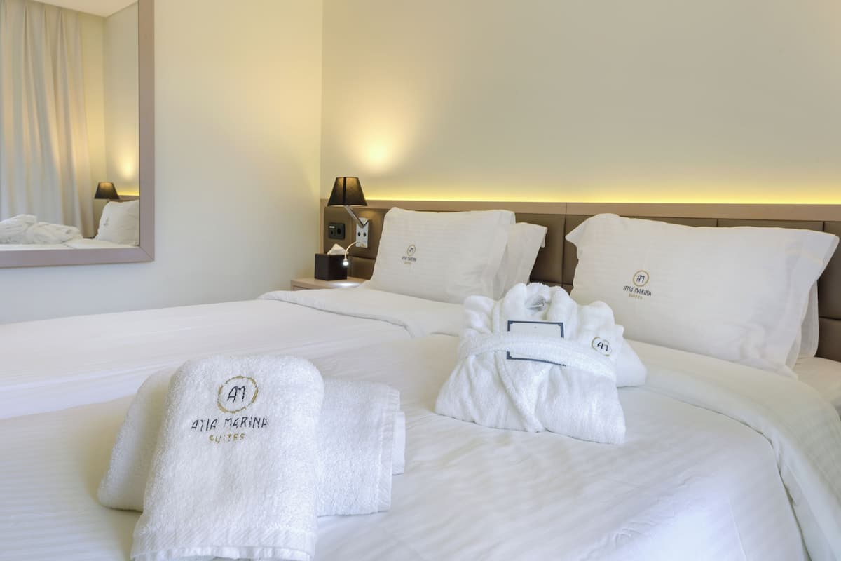Ein Hotelzimmer mit einem ordentlich bezogenen Bett, einem Nachttisch mit Lampe und Handtüchern mit dem Hotelnamen.