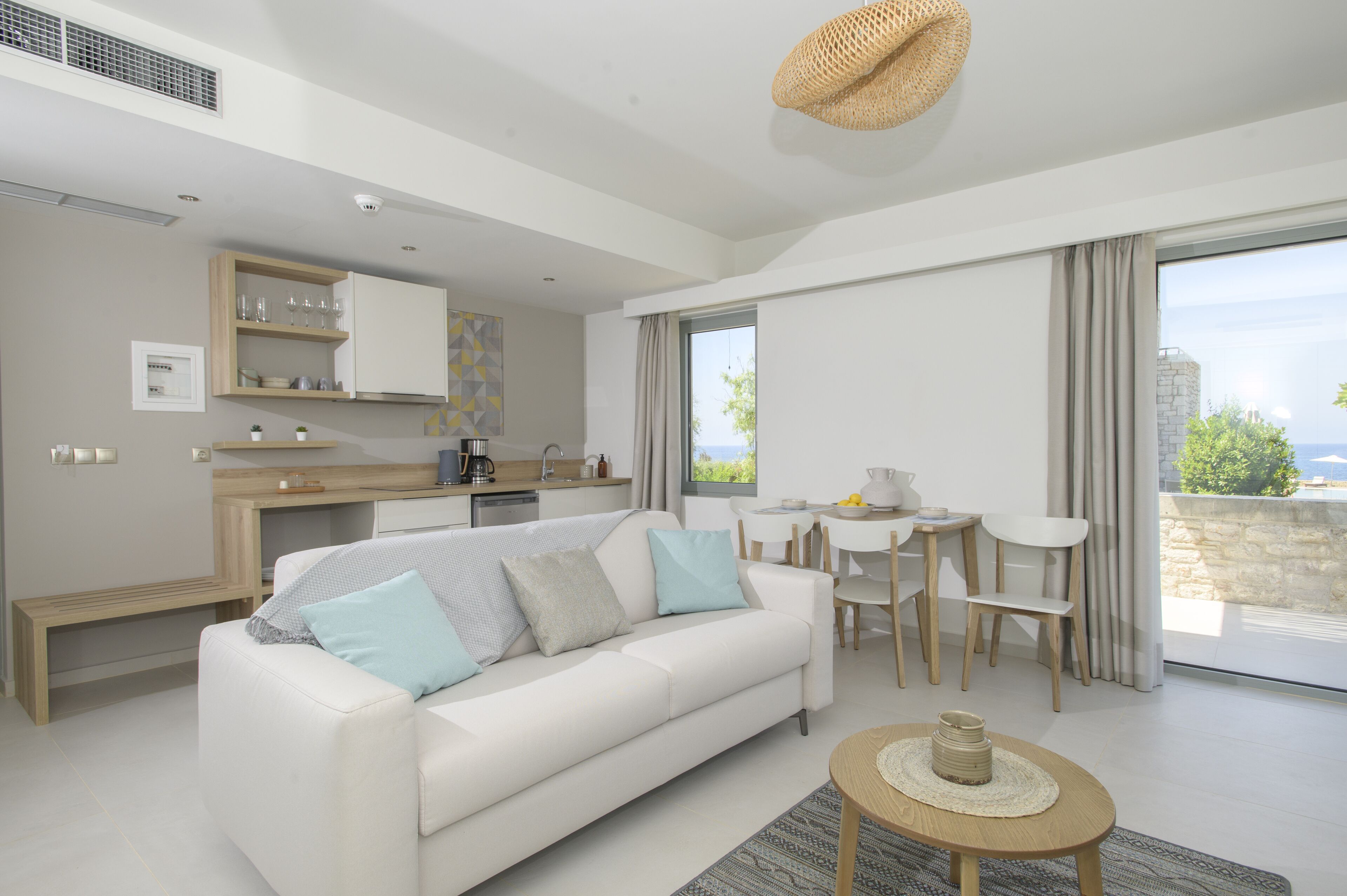 Een moderne woonkamer met een witte bank, een eethoek met een kleine tafel en een keuken met een aanrecht en kastjes.