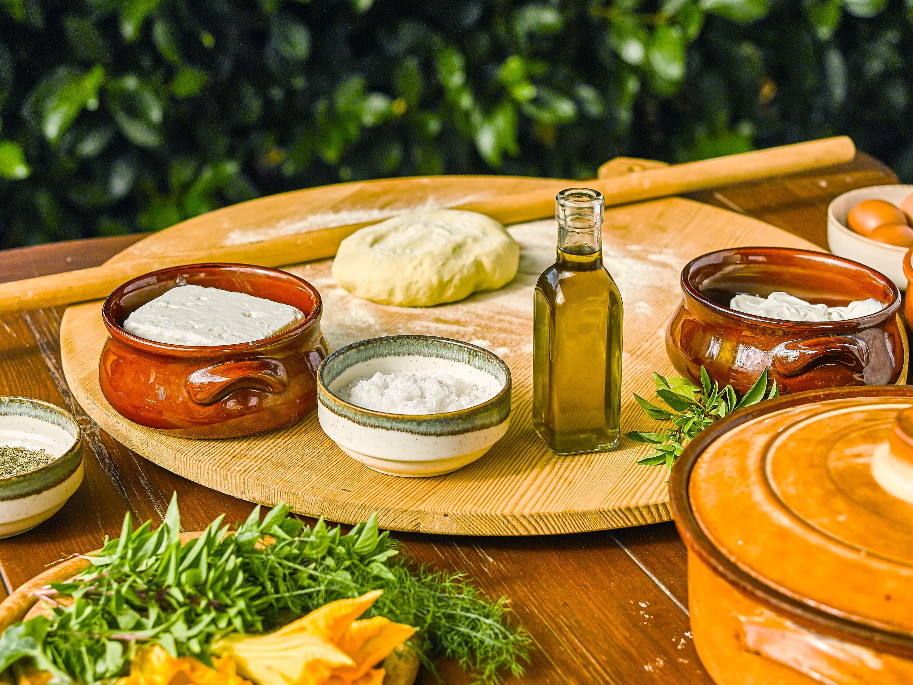 Una mesa de madera con cuencos de crema blanca, una botella de aceite de oliva y un rodillo.