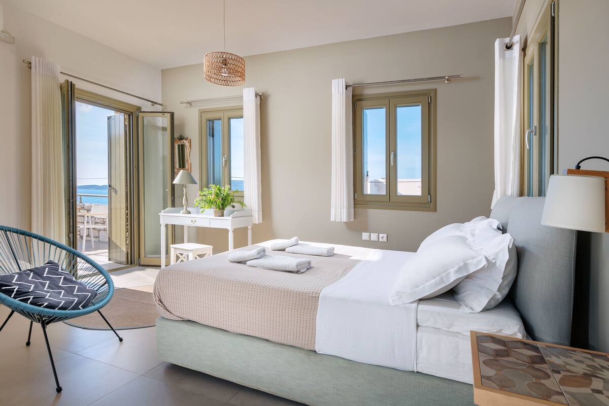 A bedroom with a bed, a chair, a desk, and a view of the outdoors.