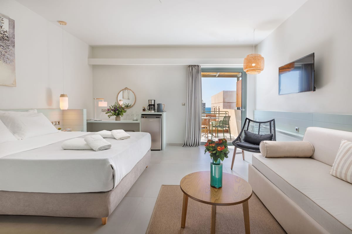 A modern hotel room with a bed, a sofa, a desk, and a view of the outdoors.