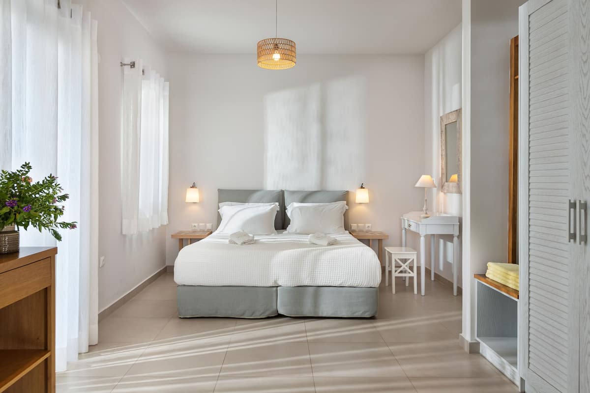 A modern bedroom with a large bed, bedside tables, a nightstand, a mirror, and a wardrobe.