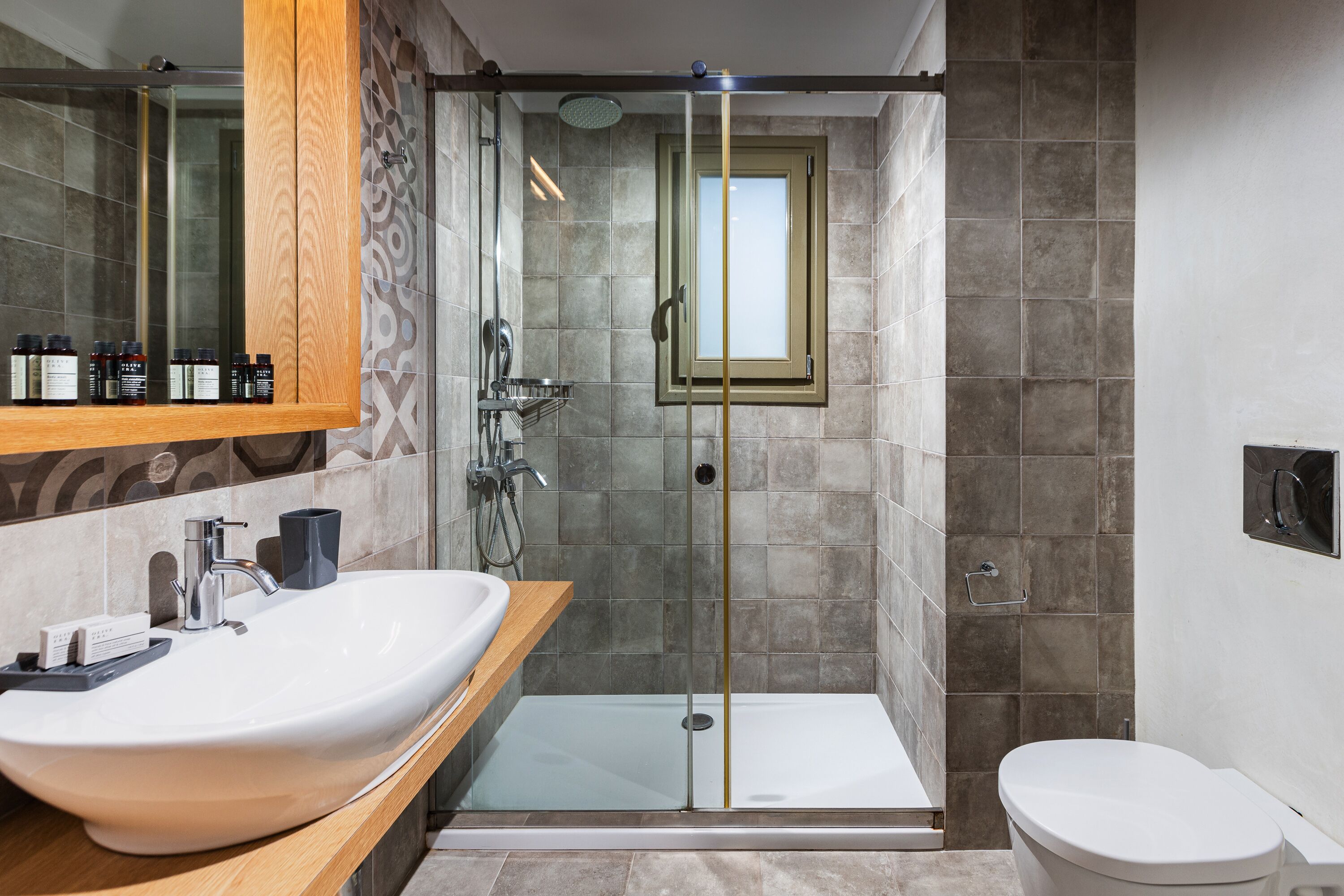 Un baño moderno con un lavamanos grande de color blanco, una ducha con cerramiento de vidrio y un inodoro.