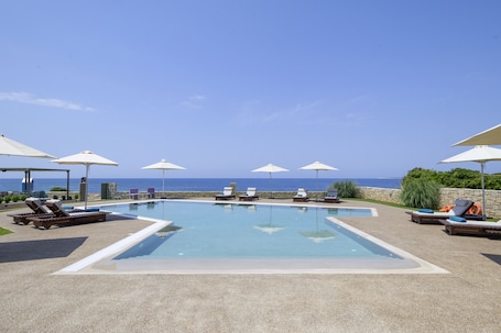 Una piscina al aire libre, sombrillas, sillones reclinables de piscina