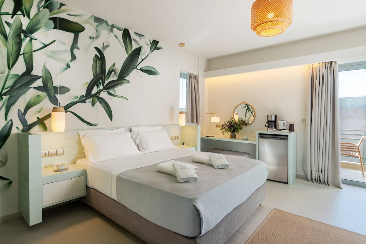 A modern hotel room with a large bed, bedside tables, a desk, and a balcony with curtains.