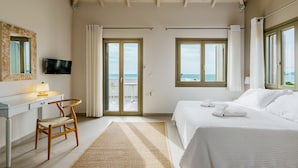 Un dormitorio con cama, escritorio, silla, televisor y vista al mar a través de las ventanas.