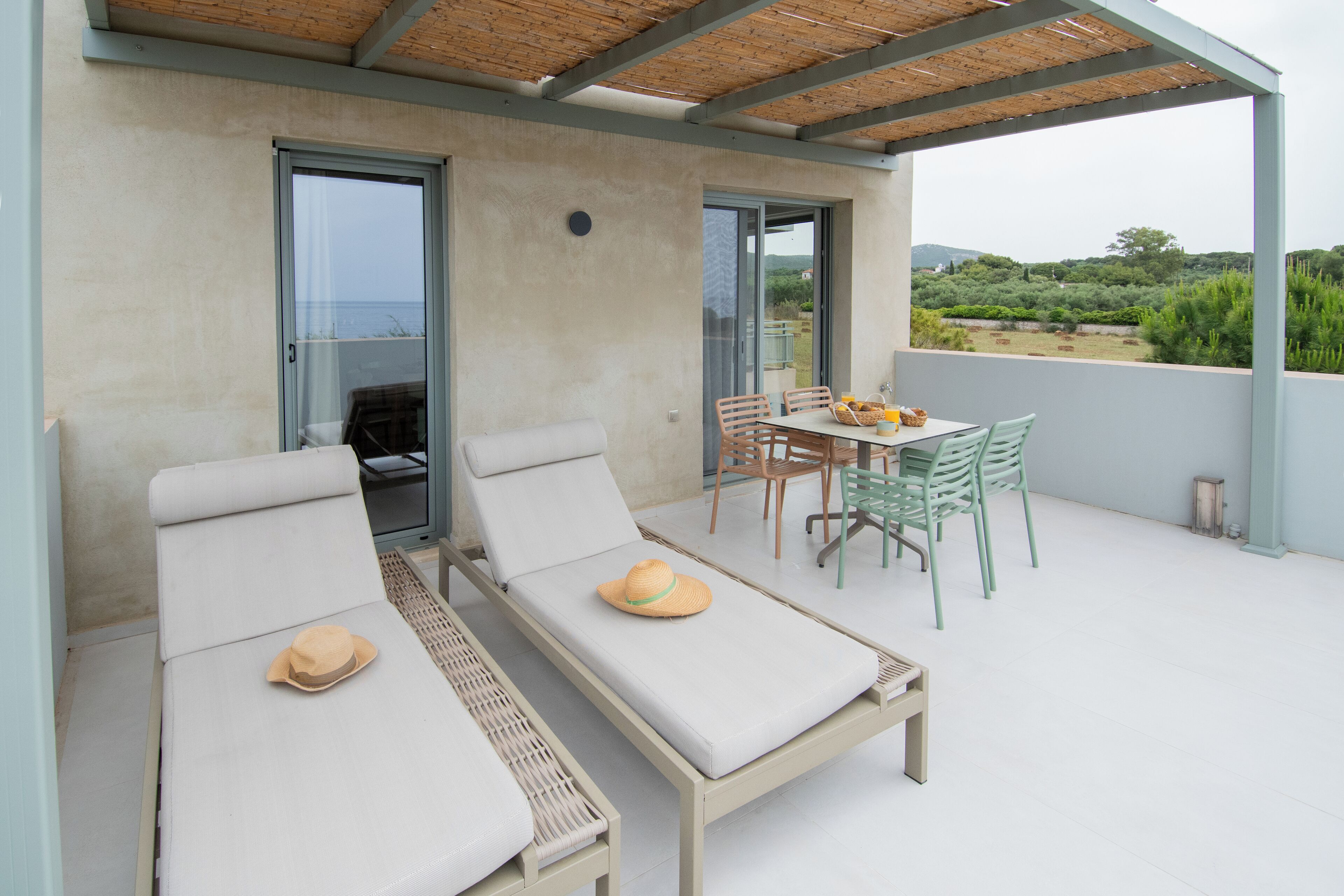 Una zona relax all'aperto illuminata dal sole, con due poltrone reclinabili, un tavolo con sedie e vista sul mare.