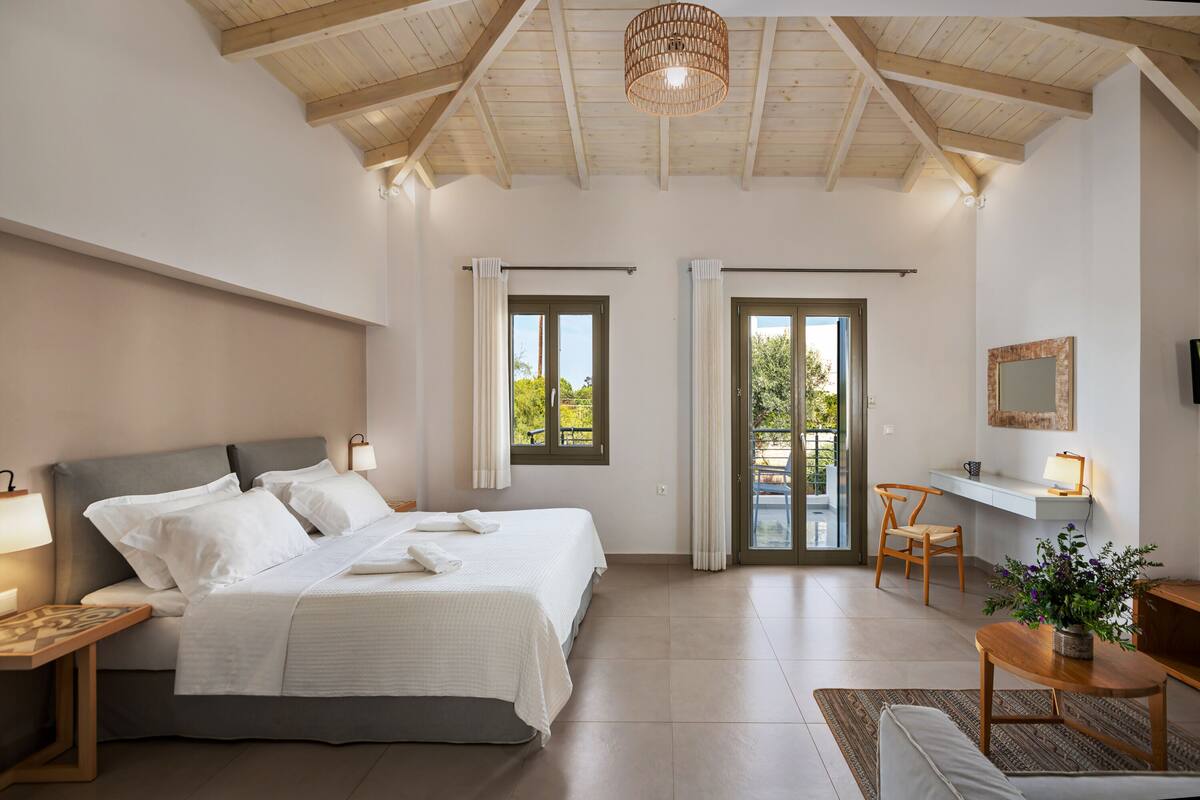 A bedroom with a bed, bedside tables, a desk, and a chair. There are windows and a door leading to an outdoor area.