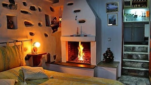 A cozy bedroom with a fireplace, a bed with pillows, and a staircase leading to a kitchen area. - Archontiko Stafylopati (Volos)