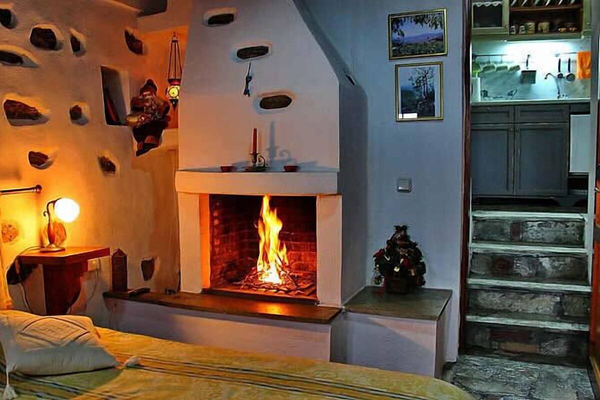 Un dormitorio acogedor con chimenea, una cama con almohadas y una escalera que lleva a una zona de cocina.