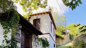 A stone-paved street leading to a white building with a wooden door and a potted plant on the steps. - Archontiko Stafylopati (Volos)