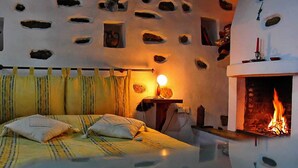 A bedroom with a bed, a bedside table with a lamp, a fireplace, and a wall with rock-like decorations. - Archontiko Stafylopati (Volos)