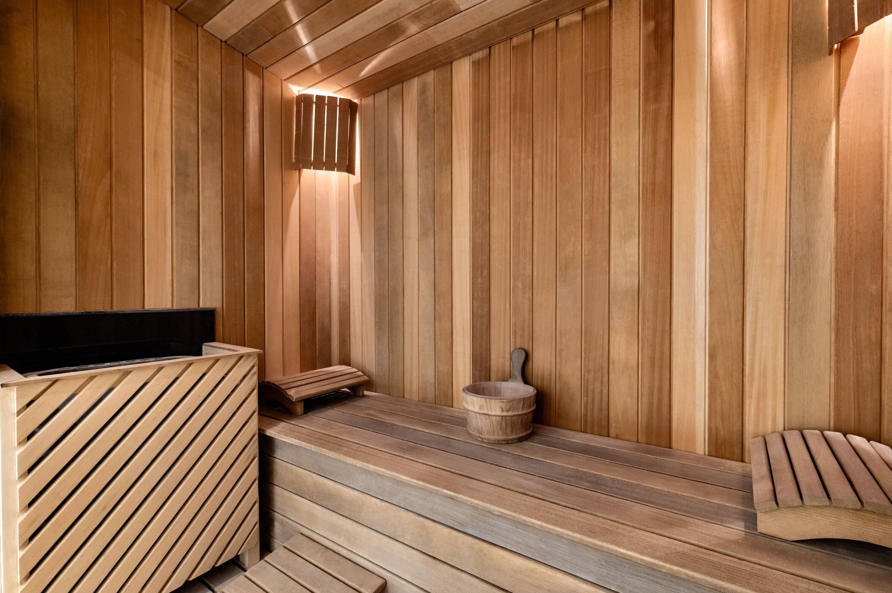 Una sauna con paredes y bancos de madera, un banco de madera con respaldo y una pileta de piedra.