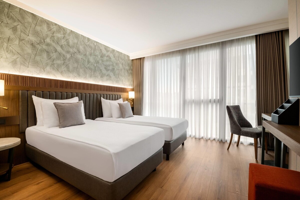 A hotel room with a large bed, a desk, a chair, and a television.