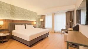 Habitación de hotel con una cama grande, un escritorio, una silla, un televisor y una ventana con cortinas.