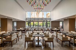 A spacious dining area with multiple tables and chairs, large windows offering a view of the cityscape, and a modern chandelier. - Ramada Encore by Wyndham Konya Selcuklu (Konya)