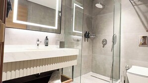 Un baño moderno con ducha envuelta en vidrio, un lavabo blanco con espejo y un inodoro.