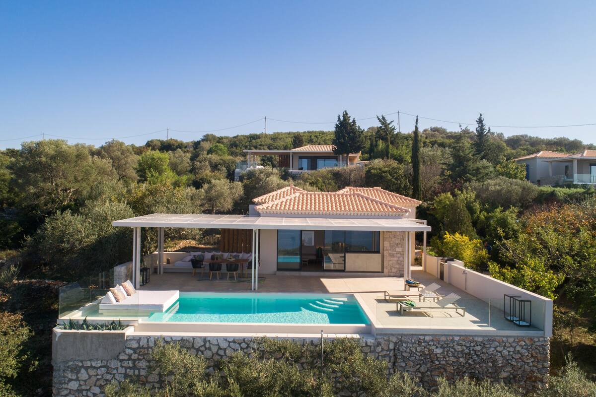 A modern villa with a swimming pool, outdoor seating, and a view of the surrounding hills.