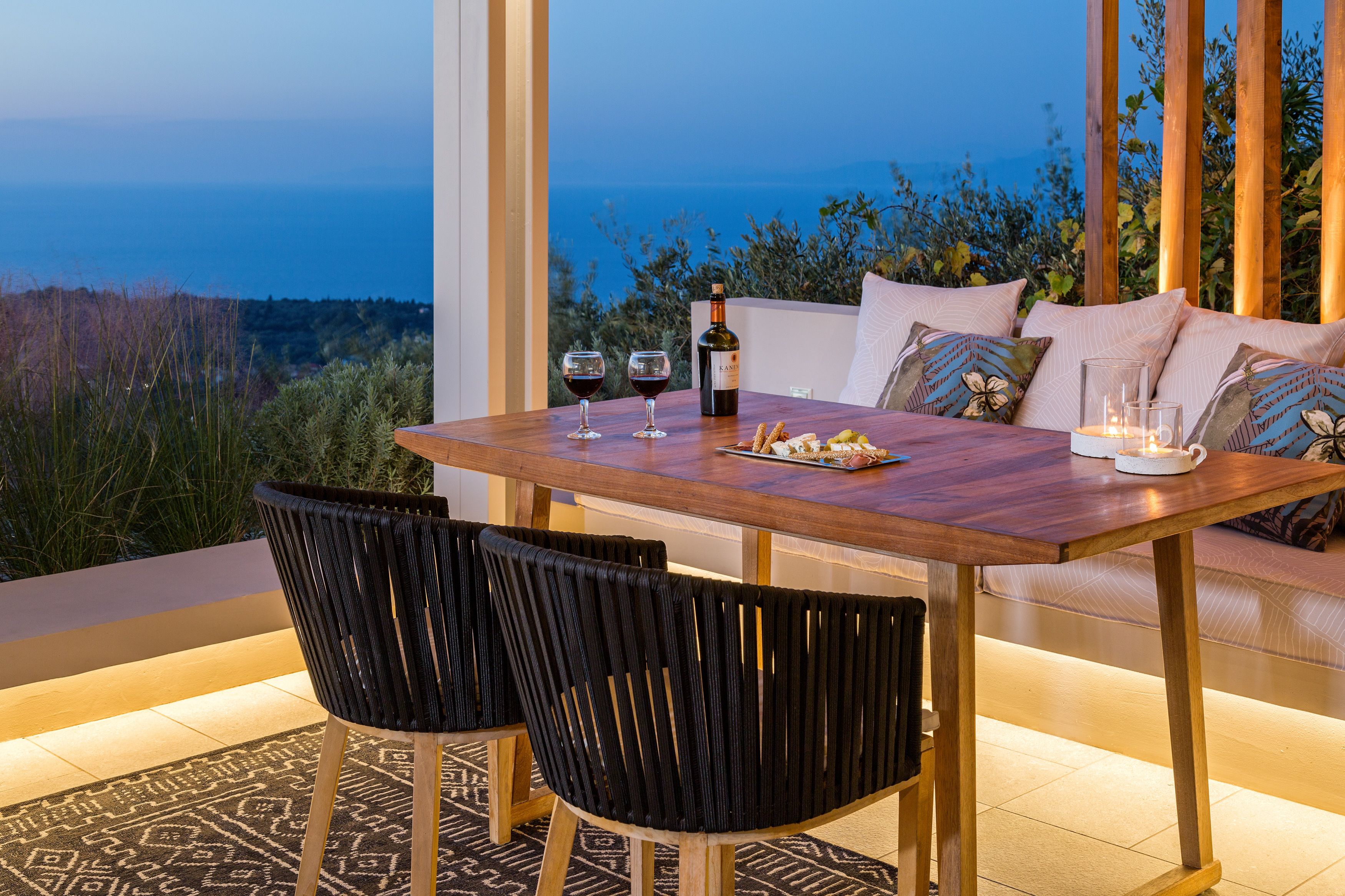 A dining area with a wooden table, black chairs, a bottle of wine, glasses, and a candle.
